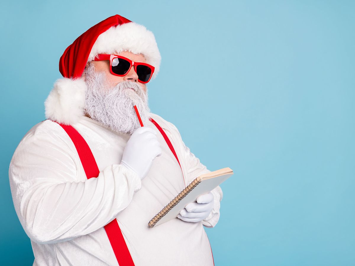 Santa plays it cool while deep in thought making a list, wearing red sunglasses that match his red suspenders