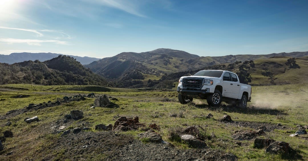 A 2022 GMC Canyon AT4 driving up a green hill.