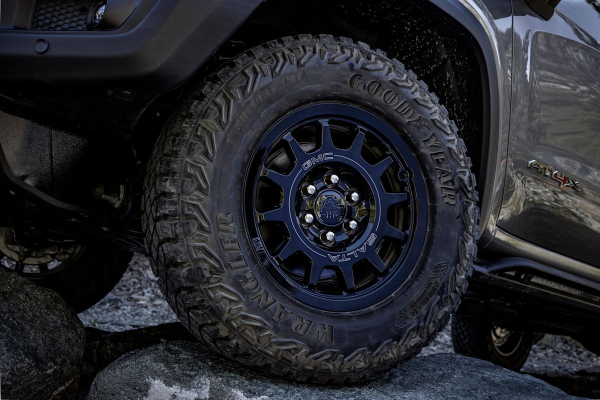 A close up of black-rimmed Goodyear tires driving over a rock. 