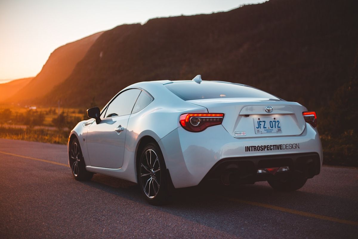 a white sedan driving down a road towards a sunset