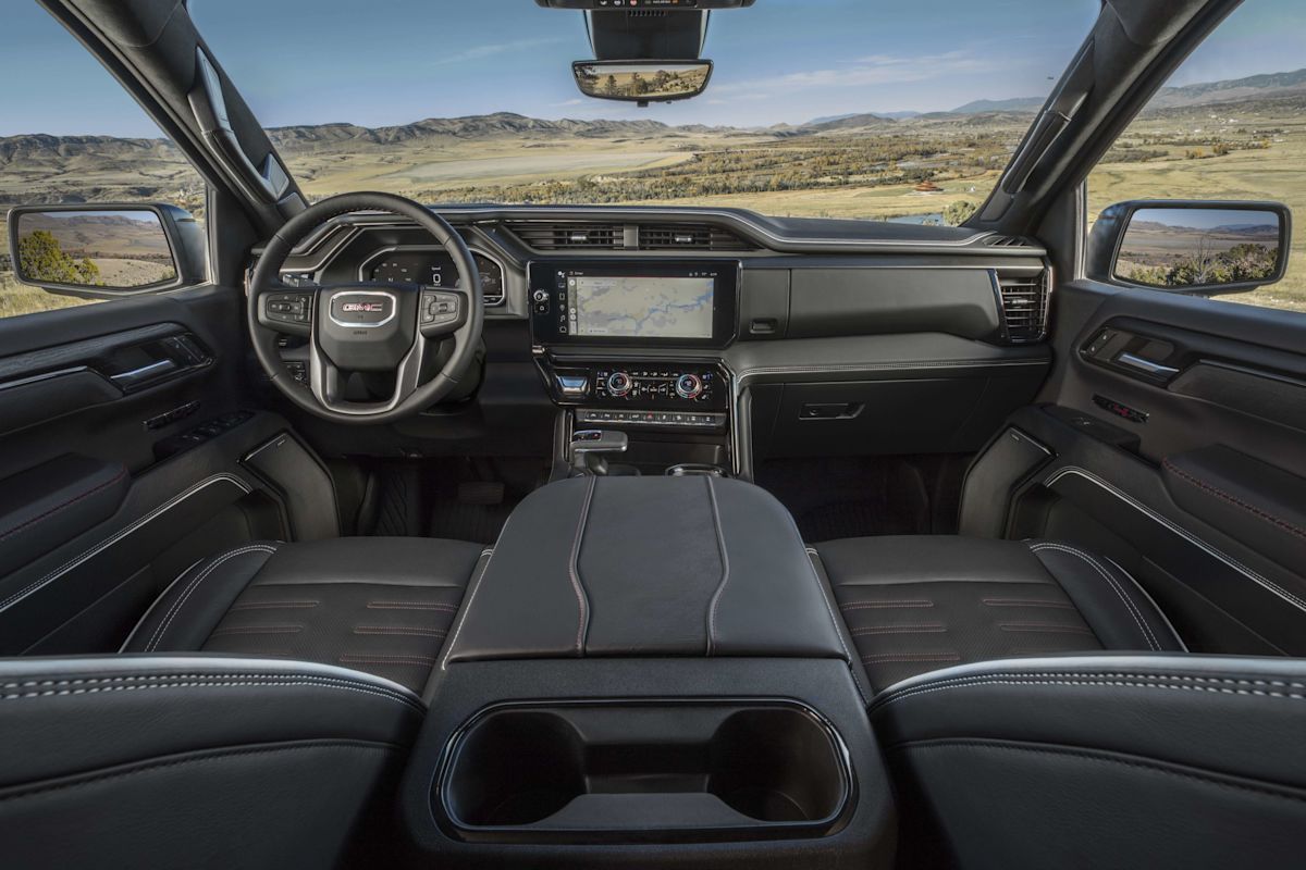 The interior view of a black leather-lined GMC SIerra 1500 with mountains high desert hills beyond.
