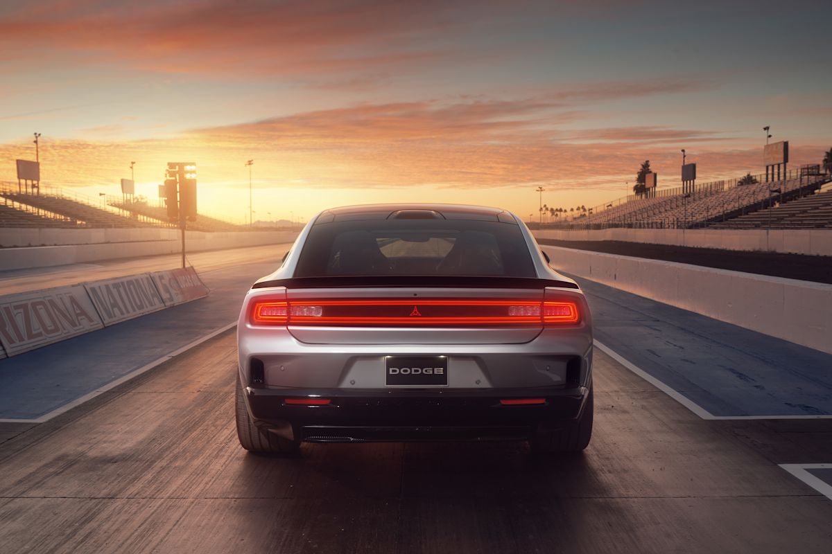 A 2024 Charger EV prepares to drive off into the multi-hued sunset, its full-width tail lights illuminated