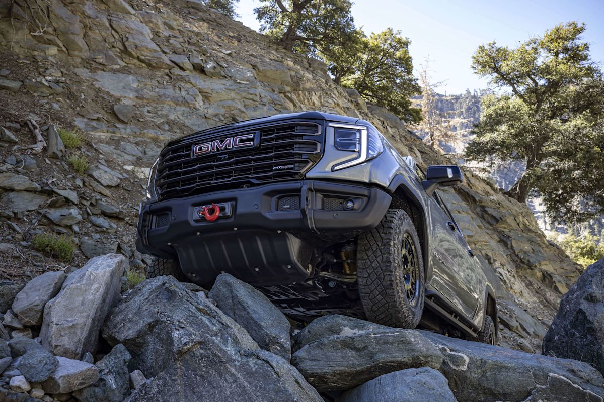 A GMC Sierra 1500 crawls over a pile of rocks with cliffs in the background. 