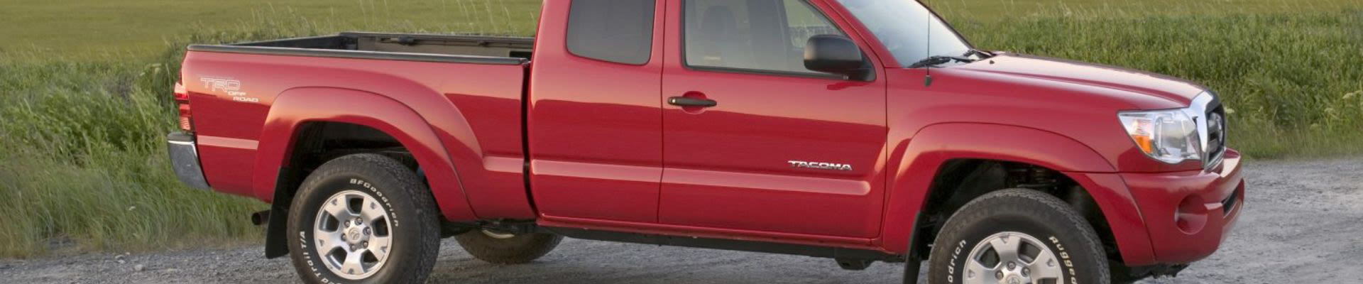 A red Toyota Tacoma parked along a grassy field