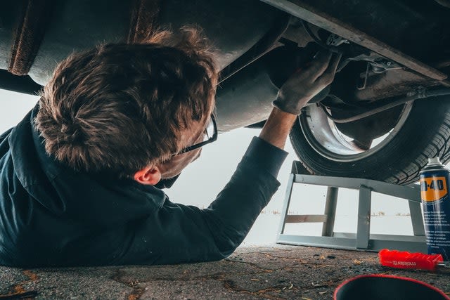 A man lays underneath his car to fix it with some tools nearby. 