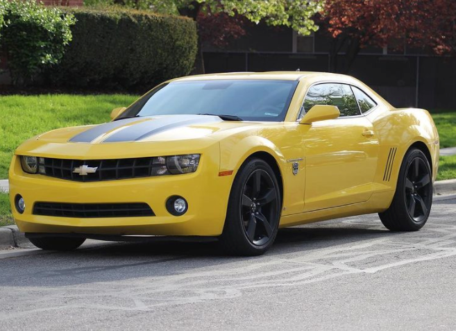 A yellow Chevrolet Camaro drives down a road. 