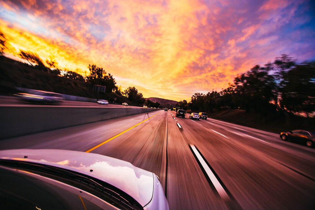 a car driving fast down a road towards a sunset