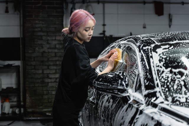 A young woman uses a sponge to wash her car. 