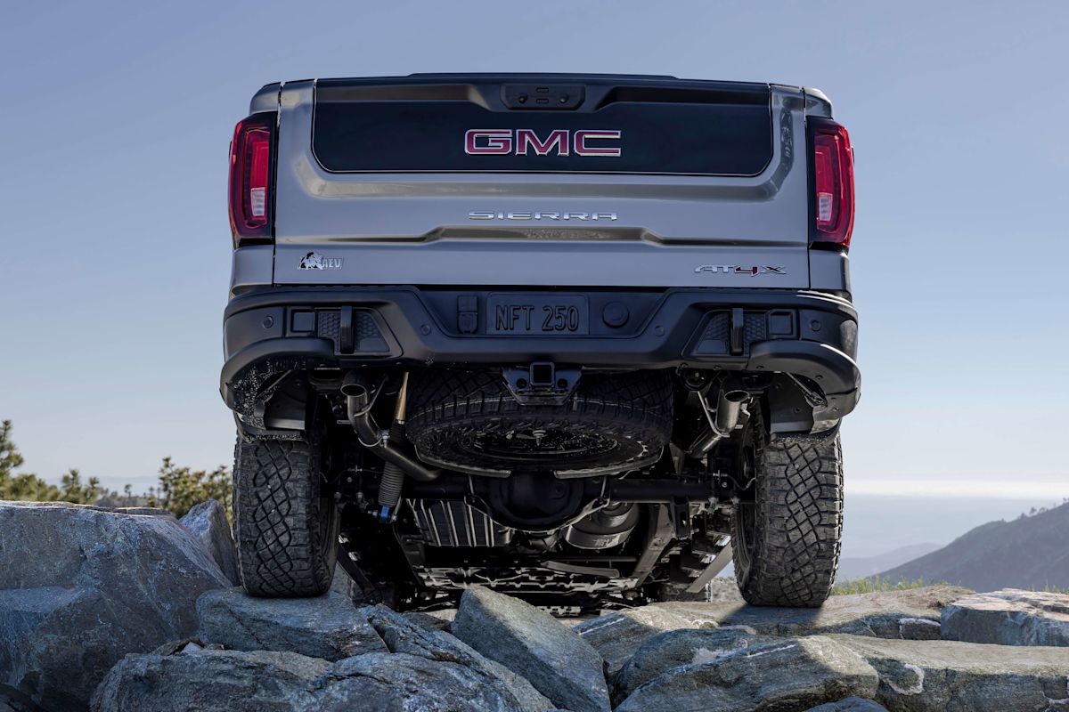 The back view of a silver GMC Sierra 1500 as it drives over rocky ground on a mountaintop.
