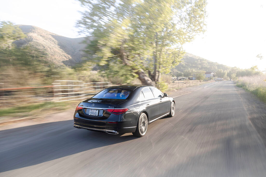 a black Mercedes-Benz S-Class driving past a green field 