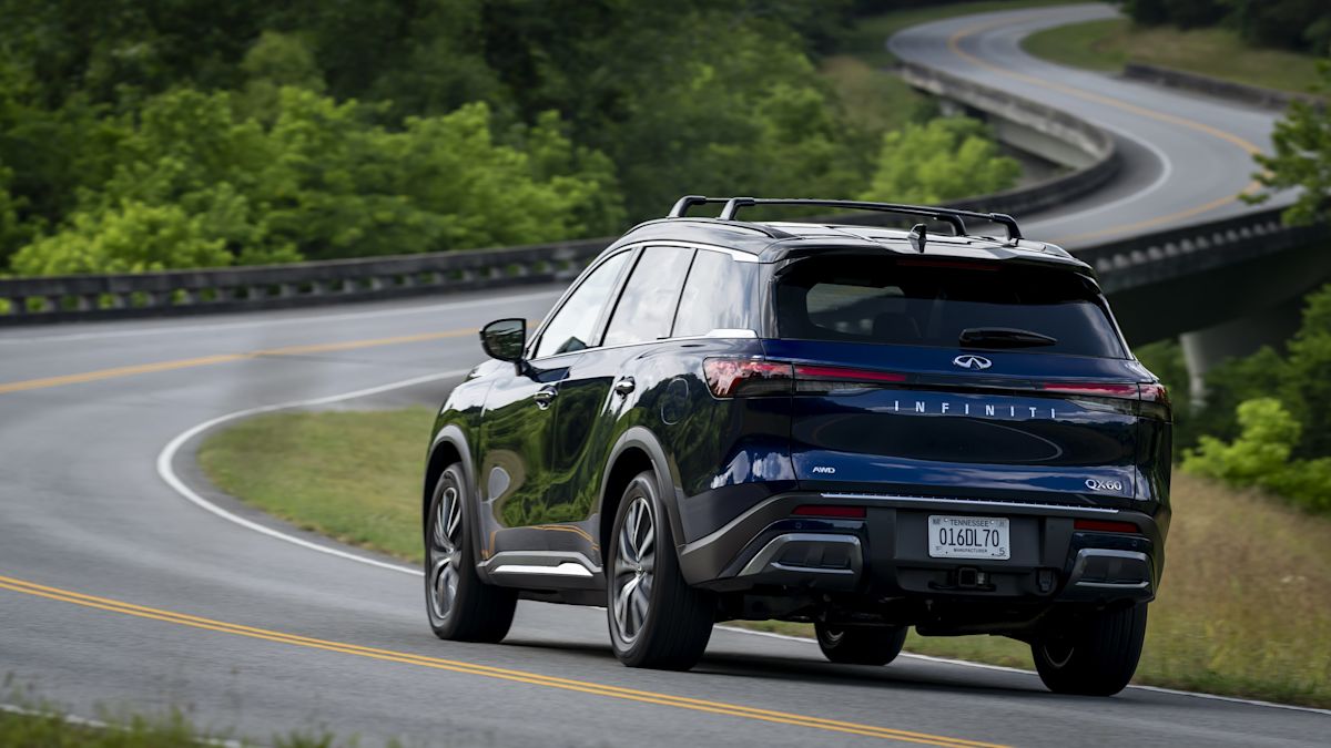 A Navy QX60 drives down a windy road approaching a bridge. Lush greenery surrounds the road. 