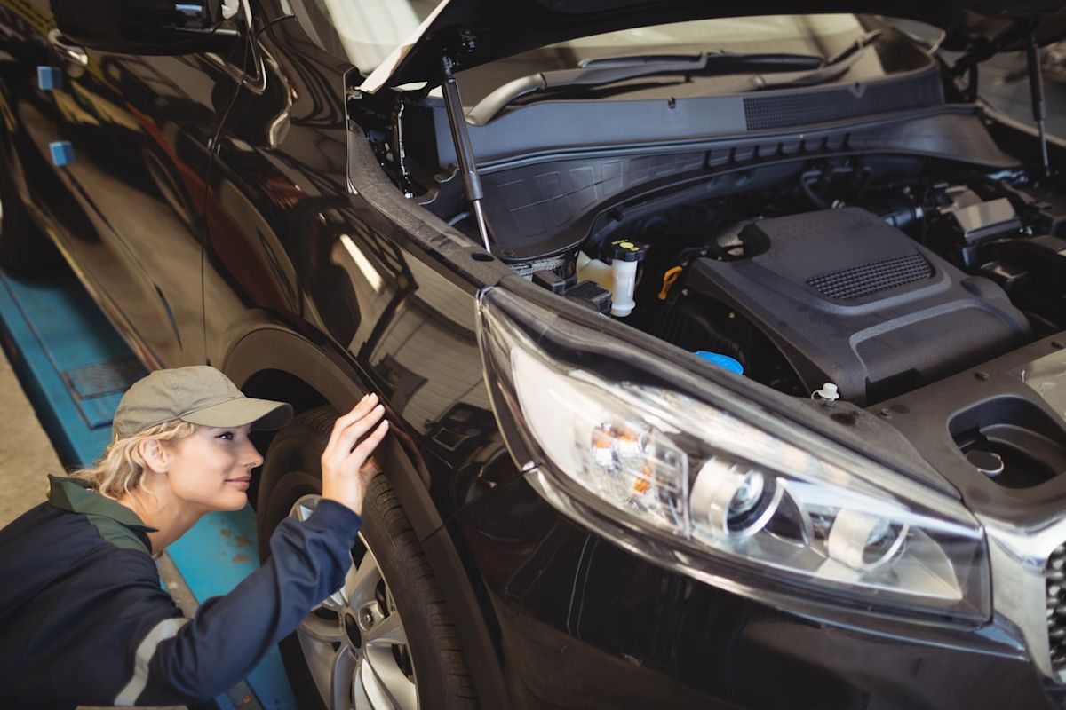 girl inspecting tire and hood of black car