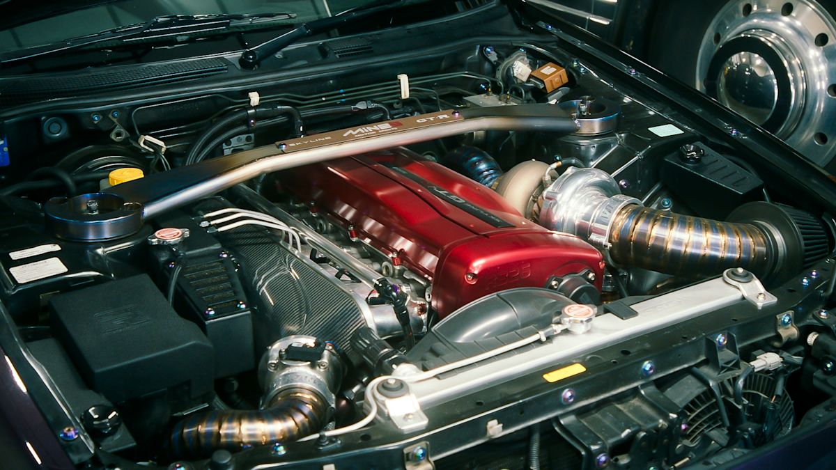 A red part stands out in the shiny silver engine compartment of a Nissan Skyline R34