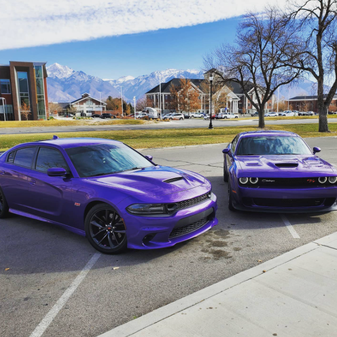 A purple Dodge Charger sits next to a purple Dodge Challenger.