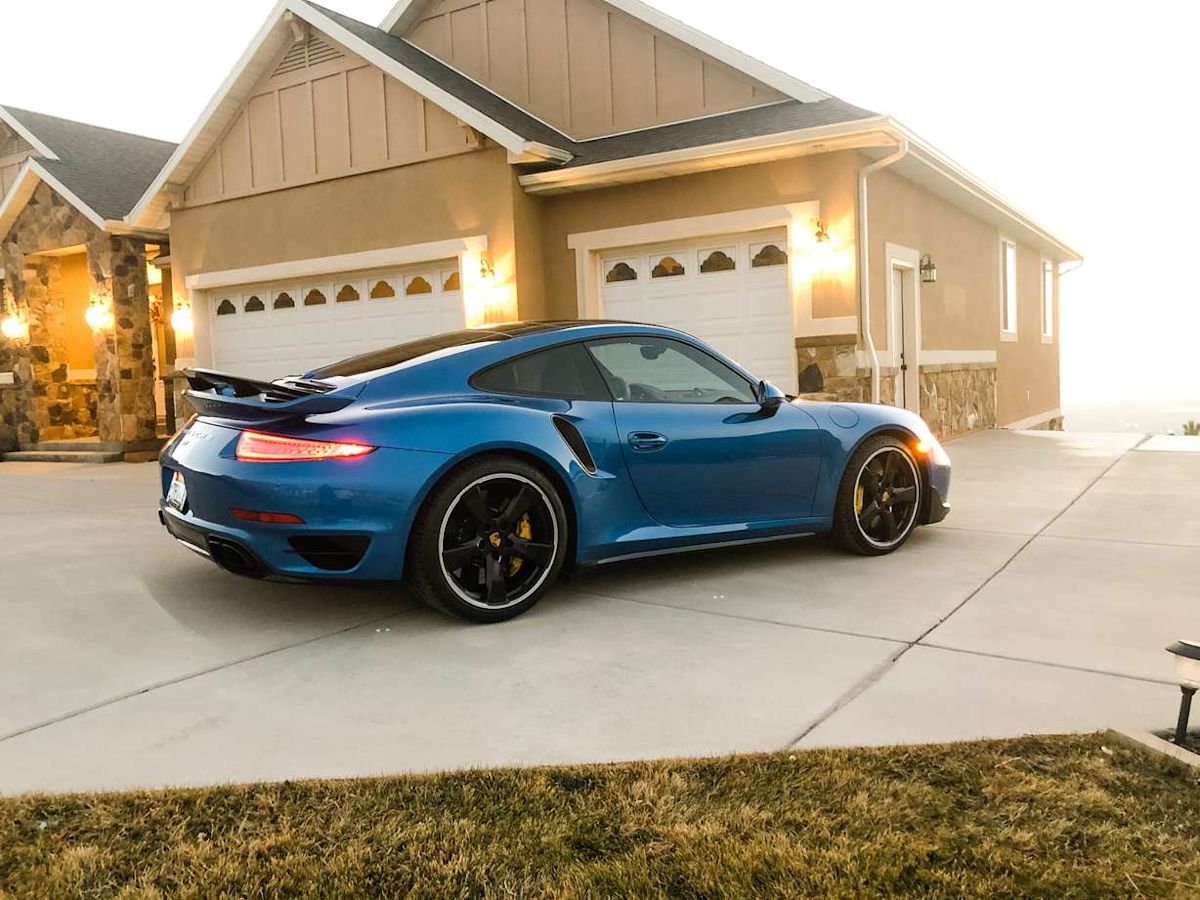 A blue Porsche 911 stands in front of a house. 