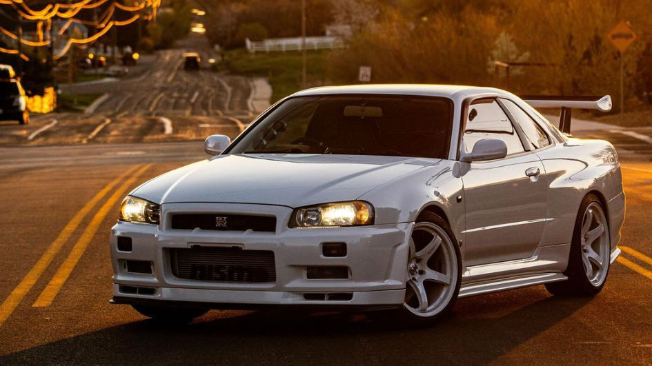 A golden setting sun illuminates the road behind a white Nissan GT-R.