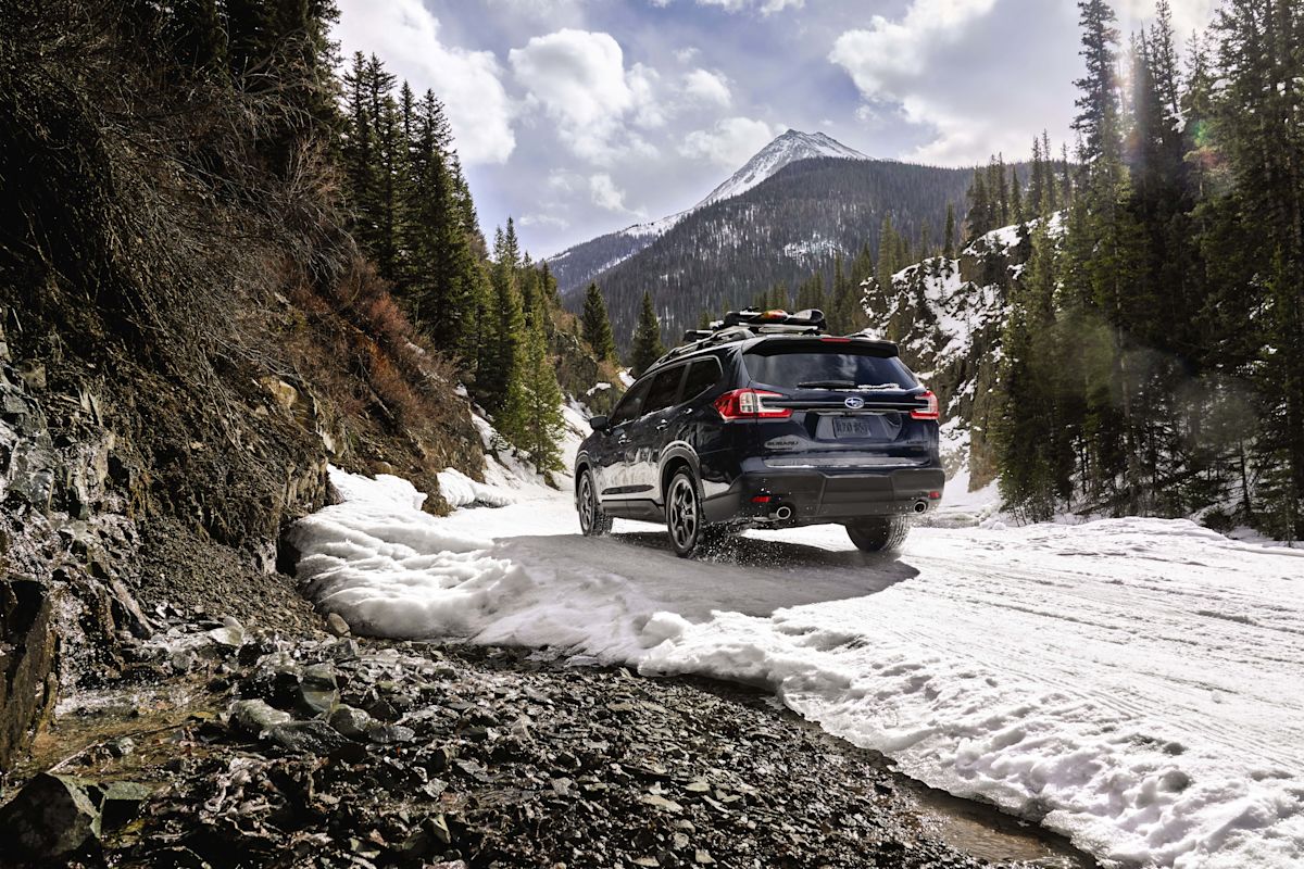 A view of the back of a blue Subaru Ascent driving toward a mountain 