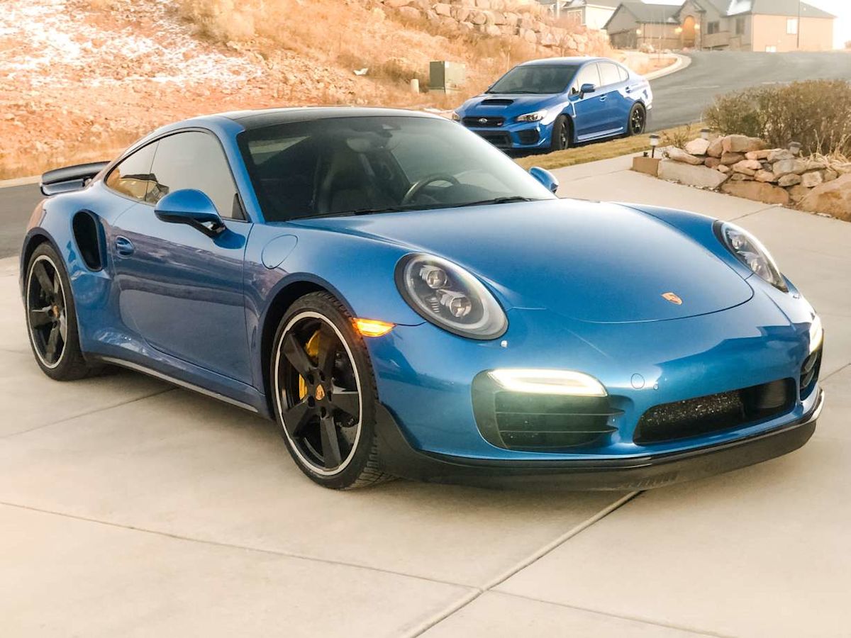 A Porsche 911 Turbo S stands in front of another blue car.