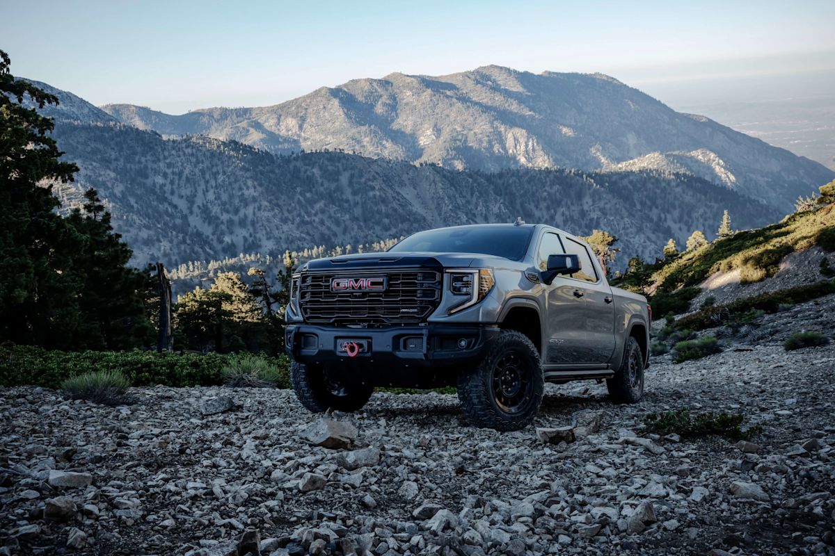 A grey GMC Sierra 1500 drives up a rugged gravel path in the mountains. 