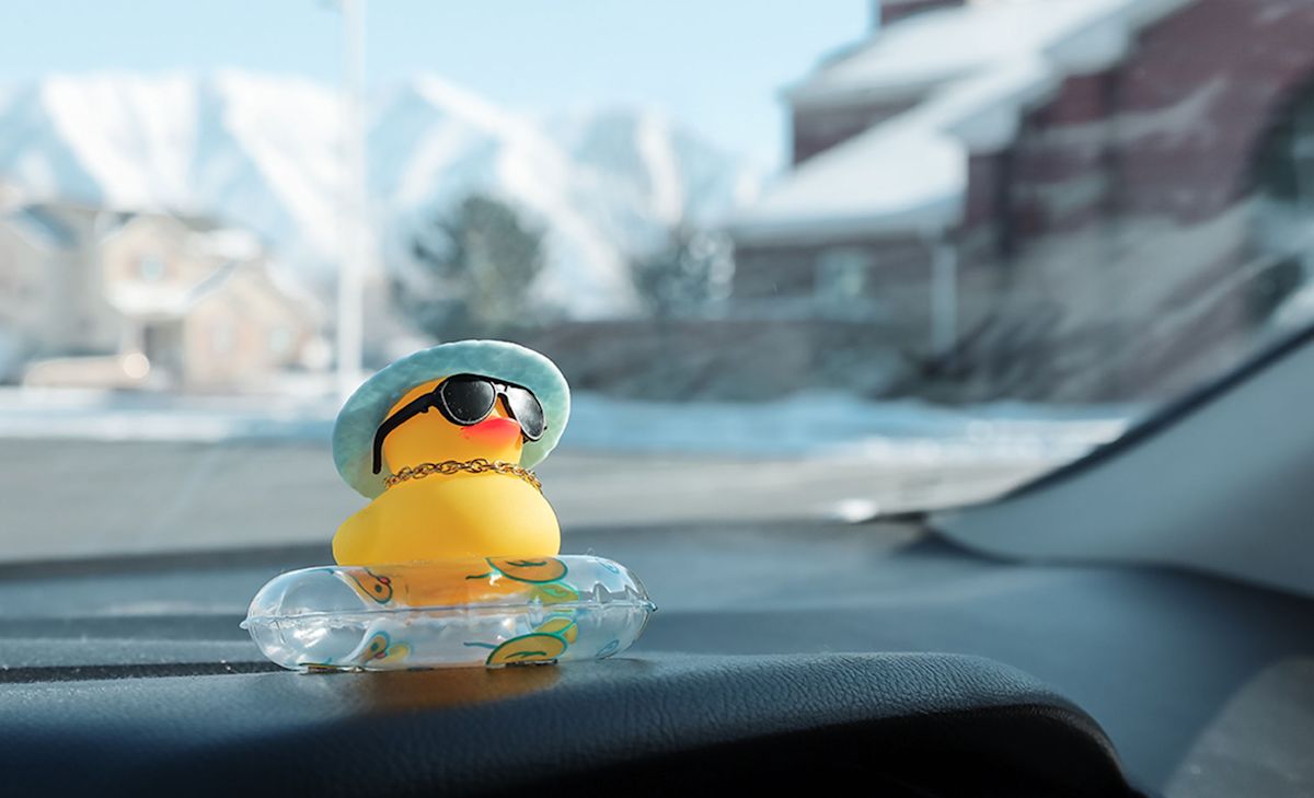 A yellow rubber duck wearing sunglasses rides on the dashboard of a Jeep.