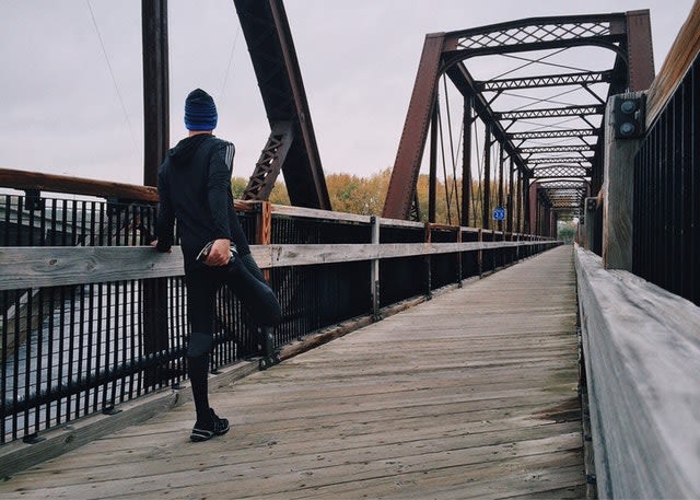 A man stretches his legs at a bridge, during a long distance race.