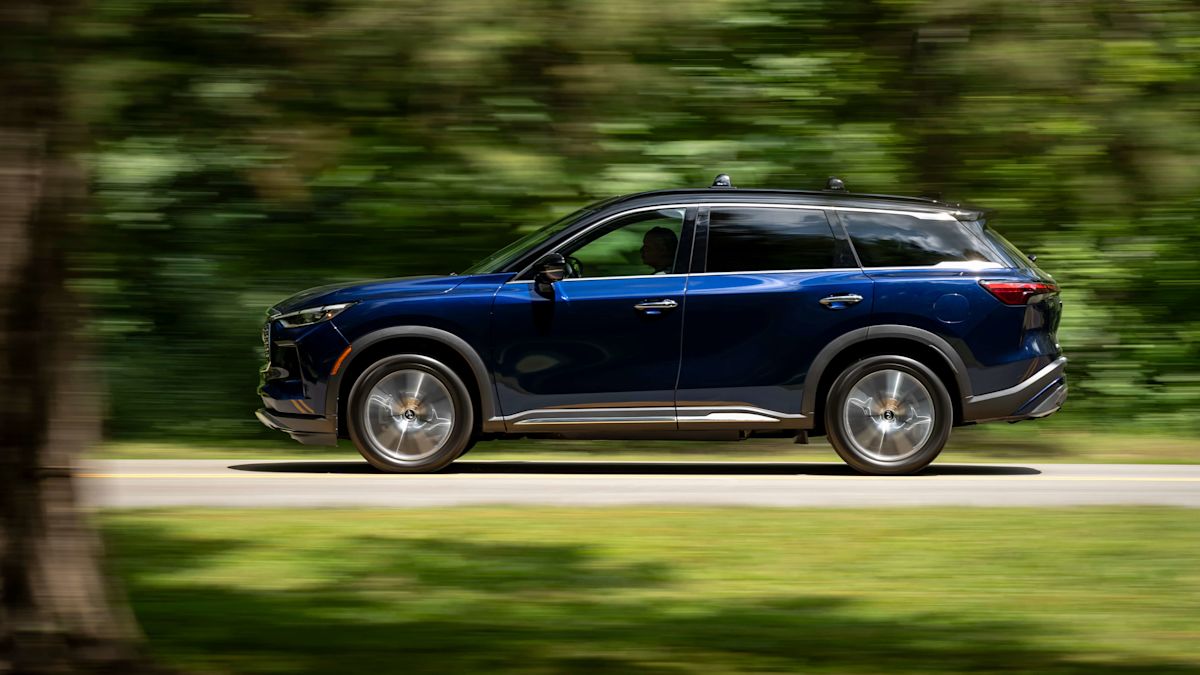 A navy QX60 drives with blurry green trees in the background. 