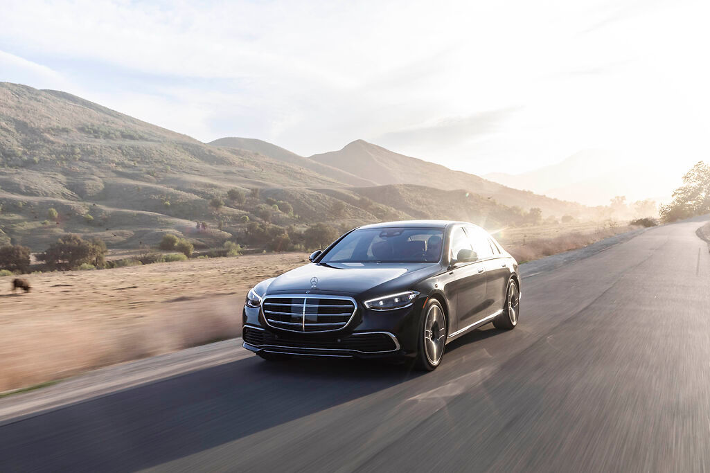 a black Mercedes-Benz S-Class driving past a green field