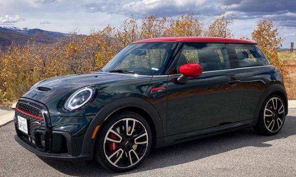 A black Mini Cooper sits in front of yellow trees. 
