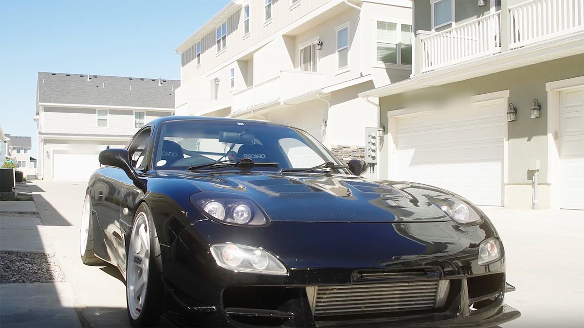 A black Maxda RX7 is parked in a townhome driveway.
