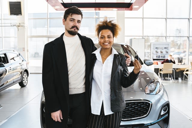 A man and woman purchase a silver car behind them. 